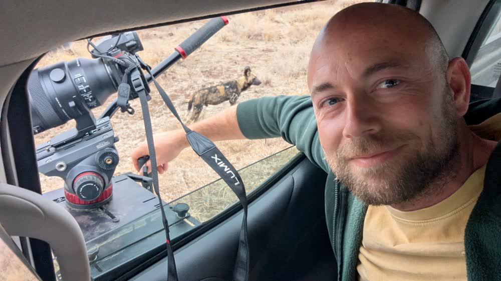 Niek in de auto, camera op statief op het raam — buiten loopt een wilde hond langs